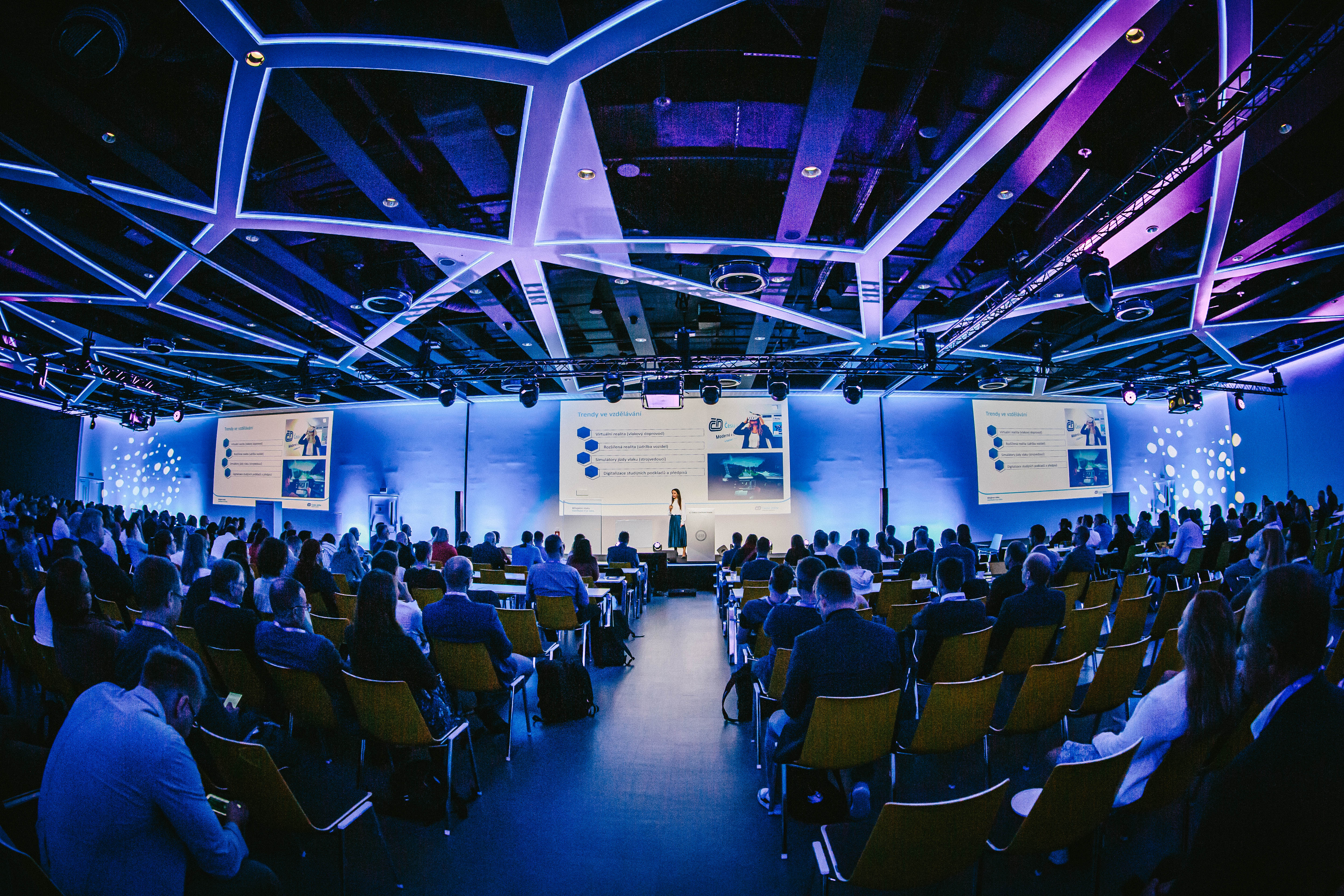 Zaplněný konferenční sál Transformation Summitu, publikum u stolů sleduje řečníky na pódiu