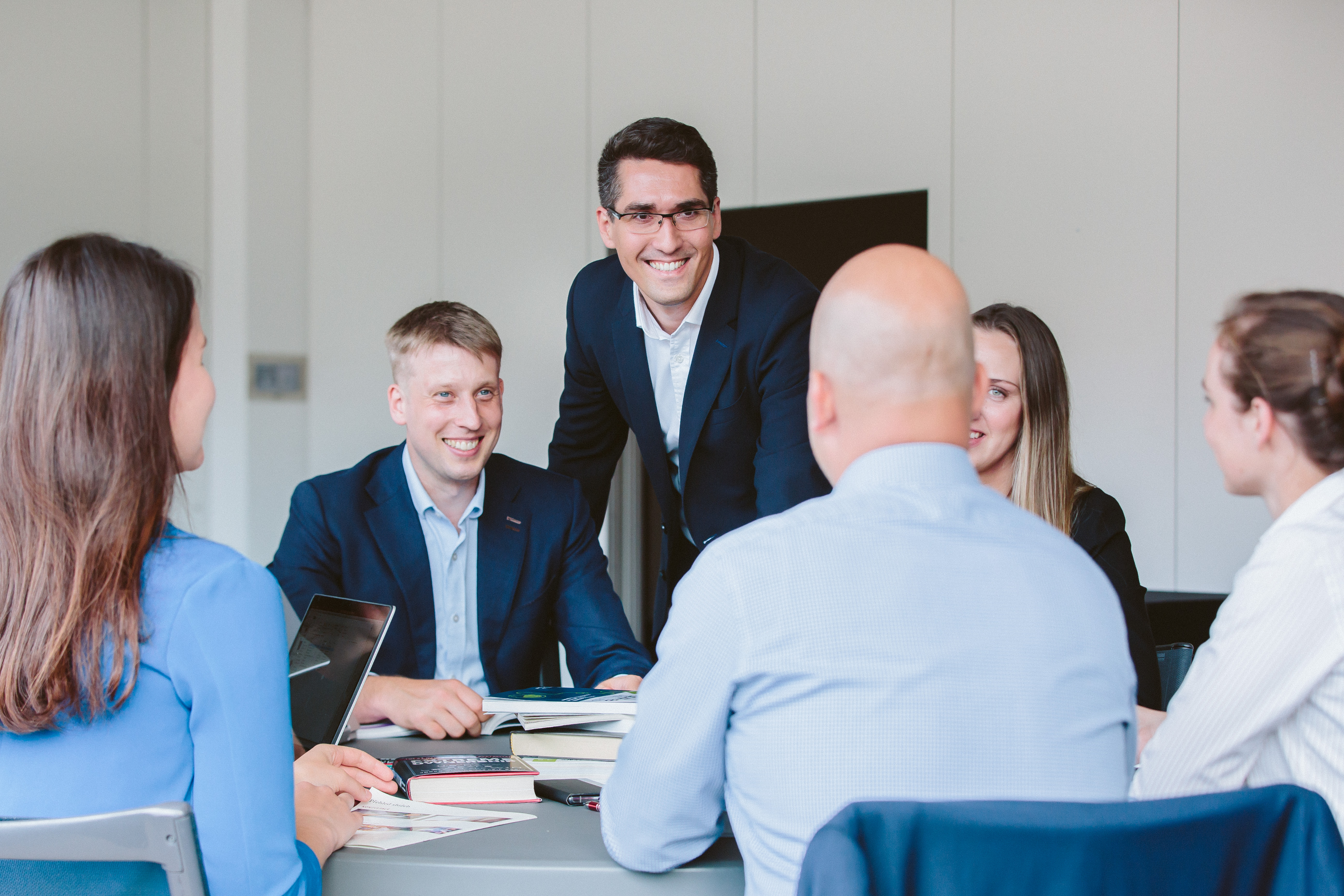 A team around a meeting table, a man standing and leading the discussion