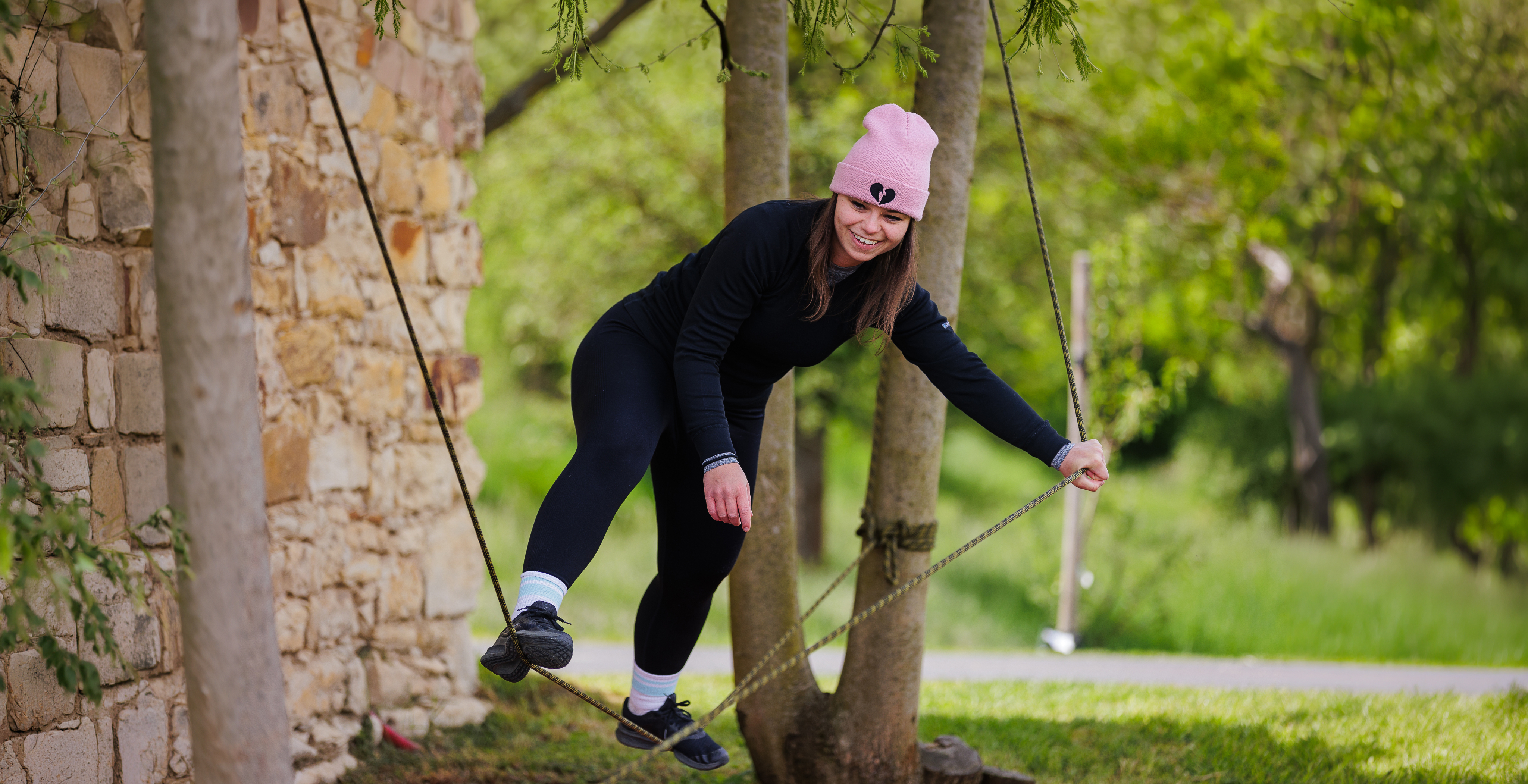 An Agile Race participant crossing a rope between trees in a park